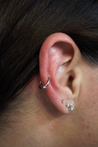 A woman's ear with three lobe piercings and a helix earring