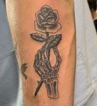 A black and white tattoo of a skeleton hand holding a rose