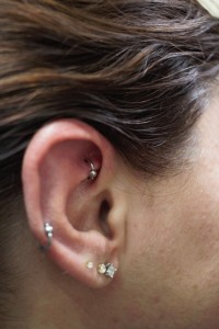 A woman's ear with a rook ear piercing, a helix ear piercing and three lobe earrings