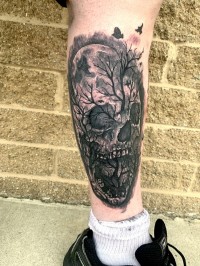 A tattoo of a skull with trees and crows
