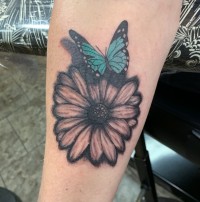 A color tattoo of a blue butterfly on a daisy