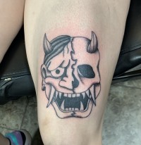 A black and white tattoo of a smiling demon face, half of which is a skull