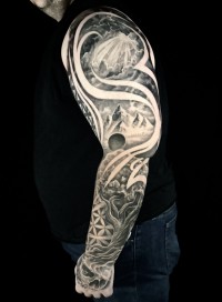 a sleeve tattoo collage of sunrays, mountains, a tree, and a skull
