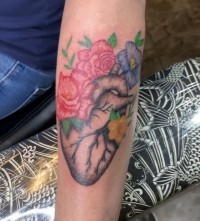 A color tattoo of a human heart adorned in flowers
