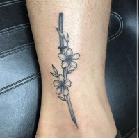 A black and white tattoo of a katana blade adorned with flowers