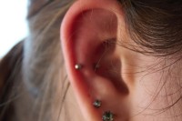 A woman's ear with two lobe piercings and a helix piercing